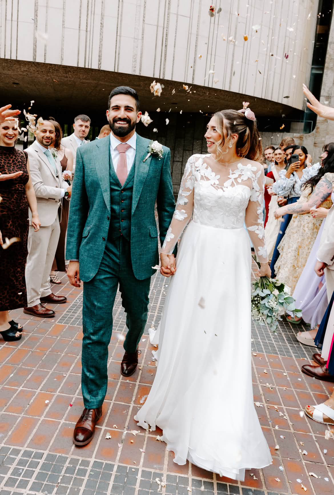 Newly married couple walking through confetti, with the groom wearing a green three-piece suit